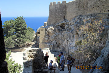 Touristen auf der Treppe der Johanniter Ritterburg bei der Besichtigung von dem Akropolis Berg von Lindos und der Insel Rhodos beim Griechenland Urlaub. Hier im Schatten ruht man sich erst mal aus und lässt seinen Blick über den schönen Hafen und Strand schweifen.